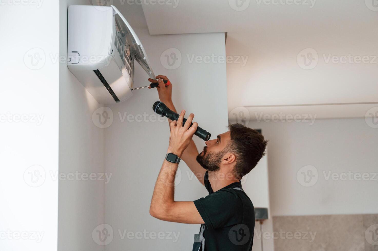 Using screwdriver ,and flashlight., Man repairs an air conditioner indoors at home photo