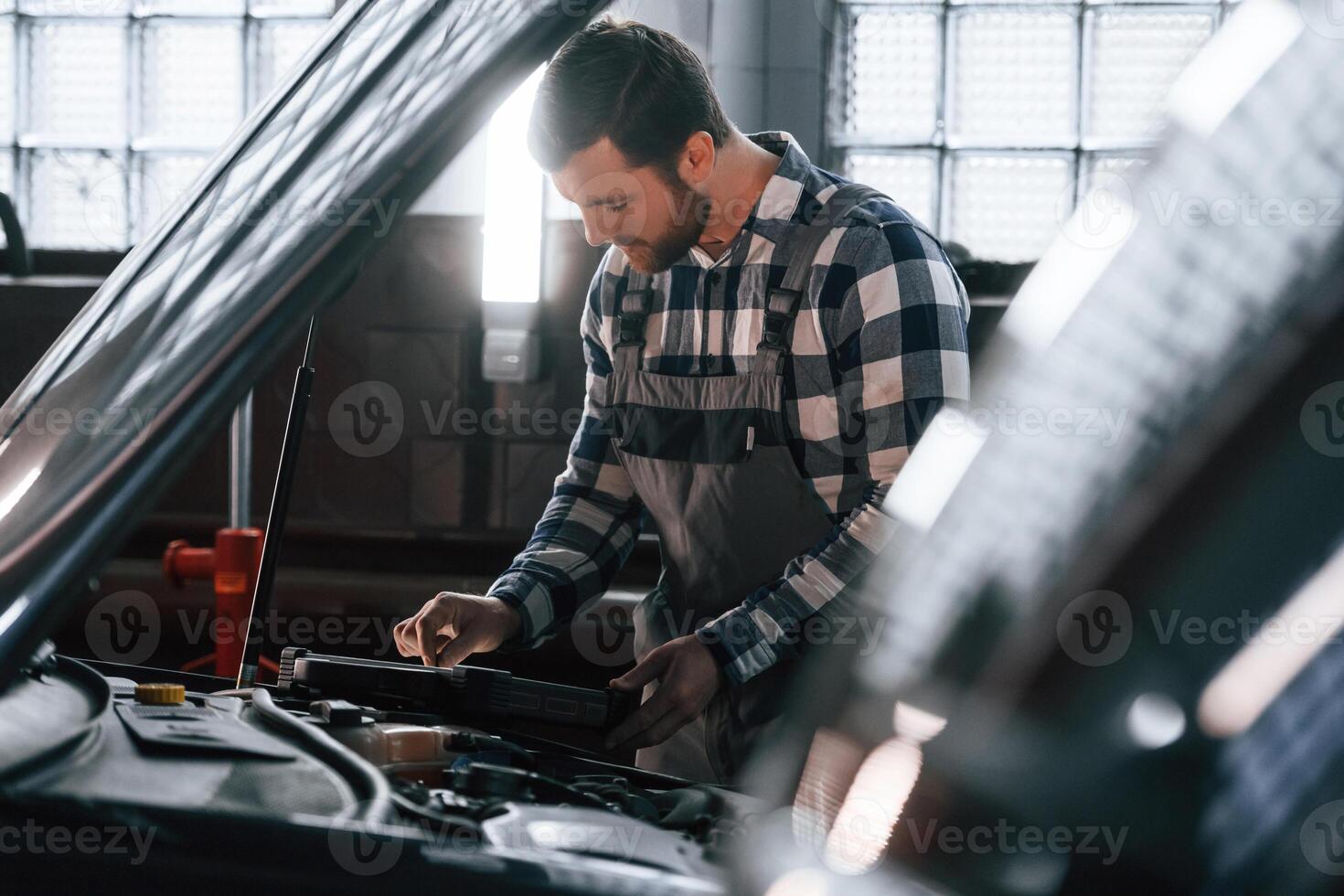 Hood of the car is opened. Using tablet. Man in uniform is working in the auto salon photo