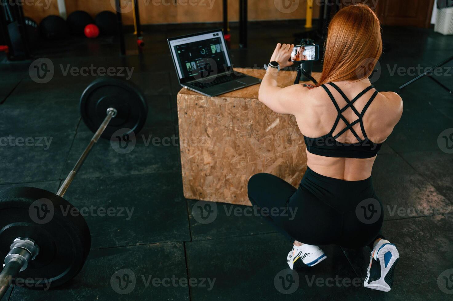 Setting ,up smartphone on, the tripod. Beautiful strong woman is in the gym photo