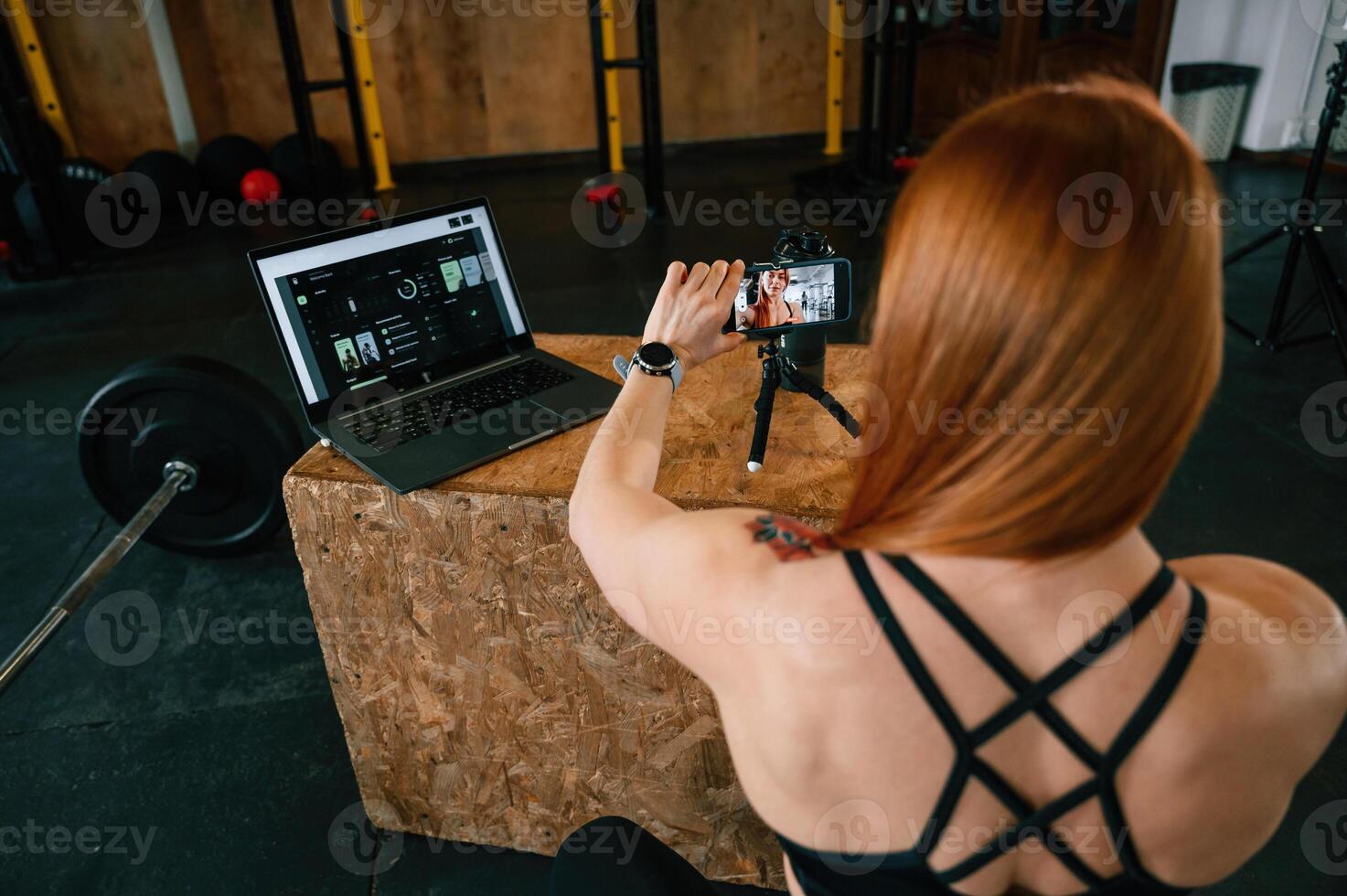 Setting up smartphone ,on ,the tripod. Beautiful strong woman is in the gym photo