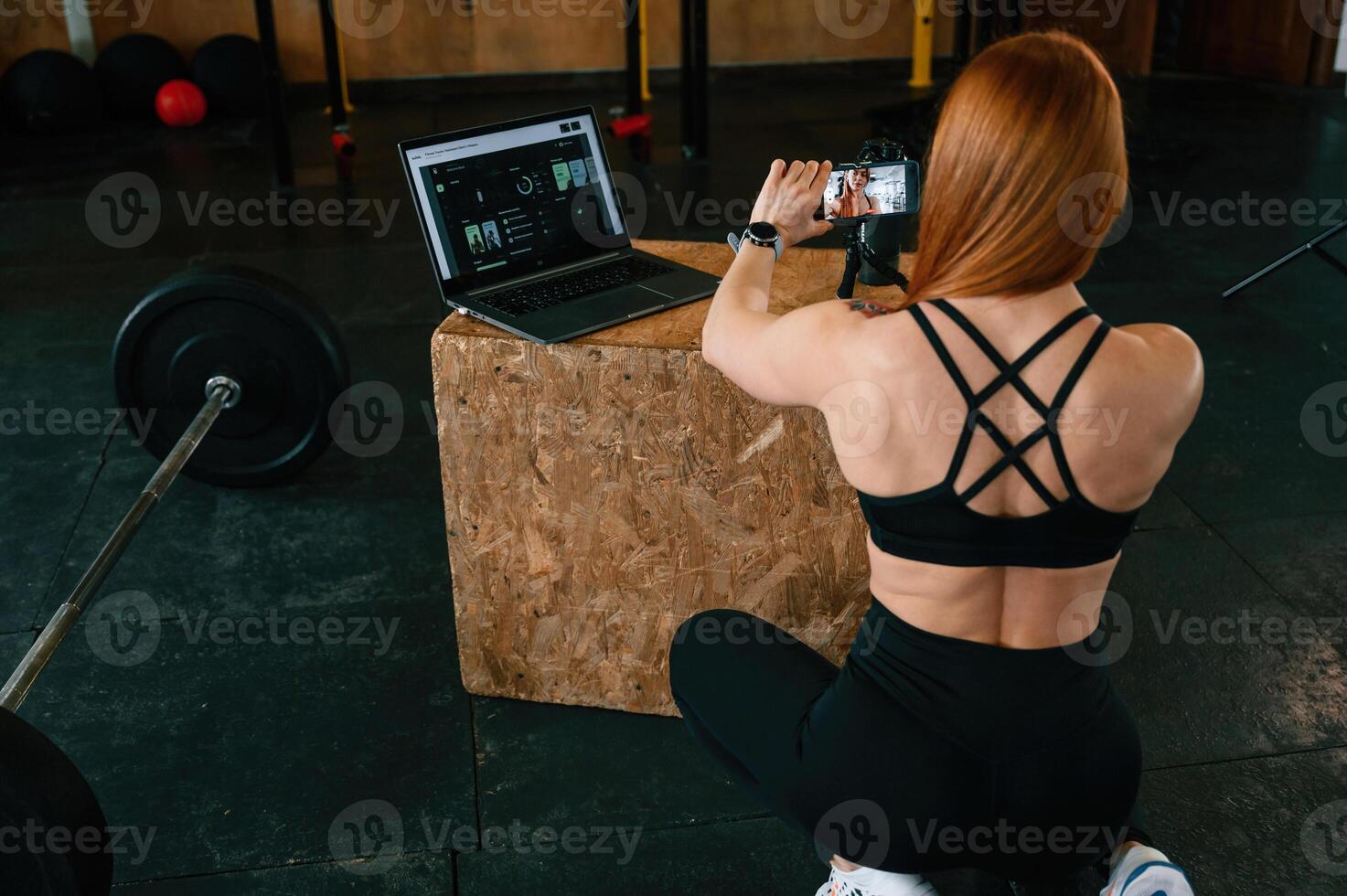 Setting up, smartphone, on the tripod. Beautiful strong woman is in the gym photo