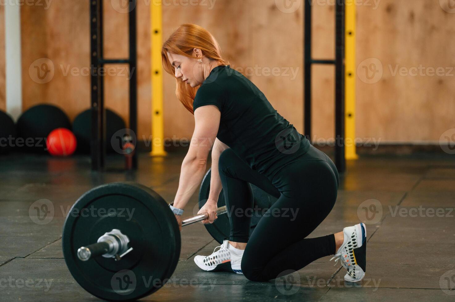 View from the side. Sitting with barbell on the floor. Beautiful strong woman is in the gym photo