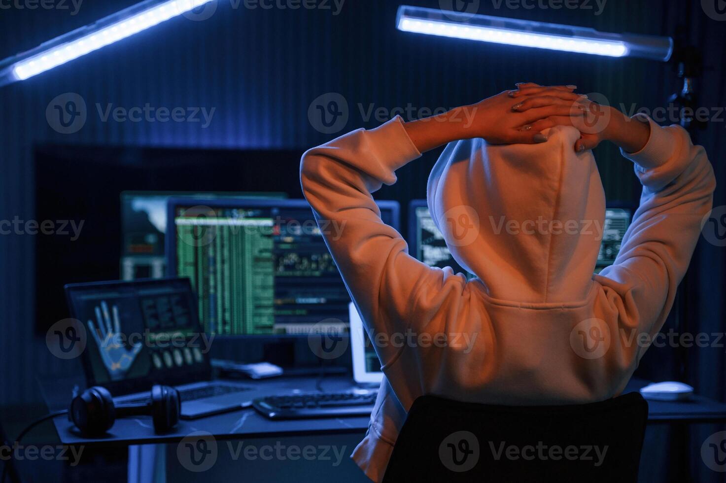Looking at screens. Young professional ,female hacker is indoors by computer with lot of information on displays photo