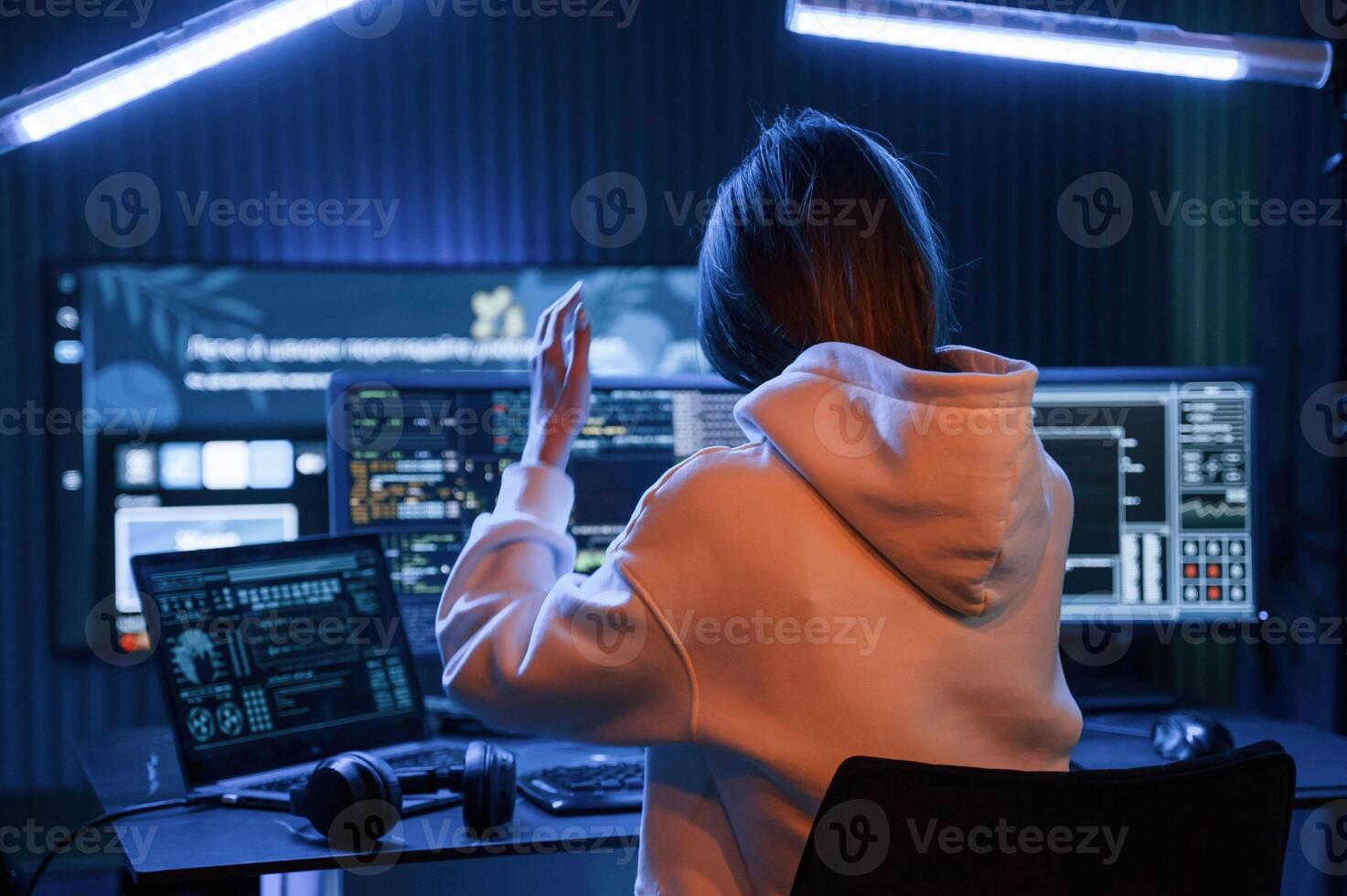 Looking, at screens. Young professional female hacker is indoors by computer with lot of information on displays photo
