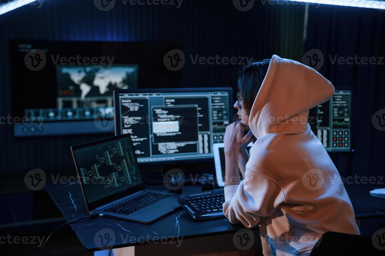 Dark, room.. Young professional female hacker is indoors by computer with lot of information on displays photo