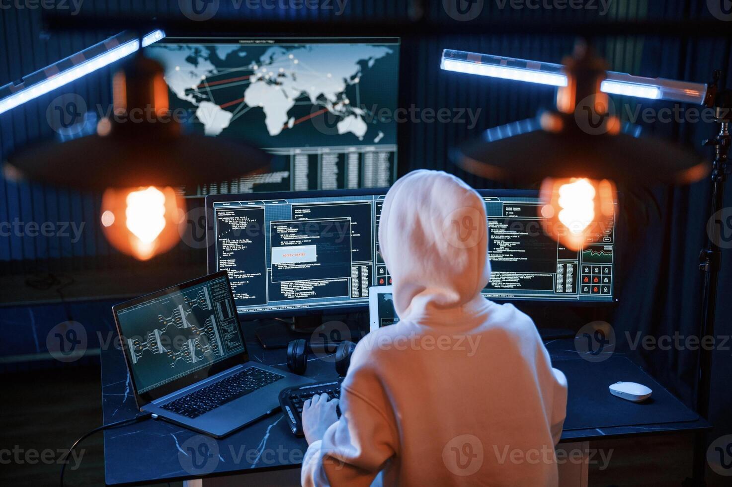 Sitting, in white hoodie. Young professional female, hacker is indoors by computer with lot of information on displays photo