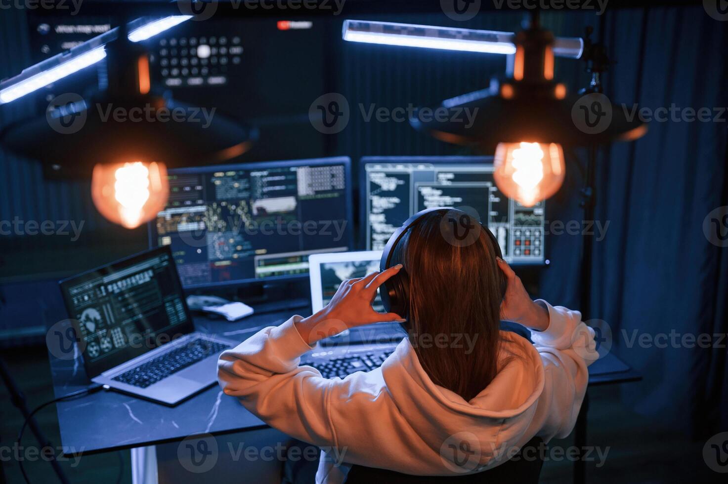 Looking, at screens. Young professional, female hacker is indoors by computer with lot of information on displays photo