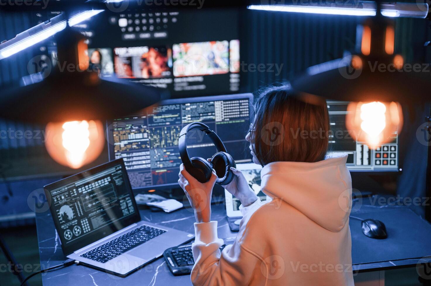 Artificial lighting,. Young, professional ,female hacker is indoors by computer with lot of information on displays photo