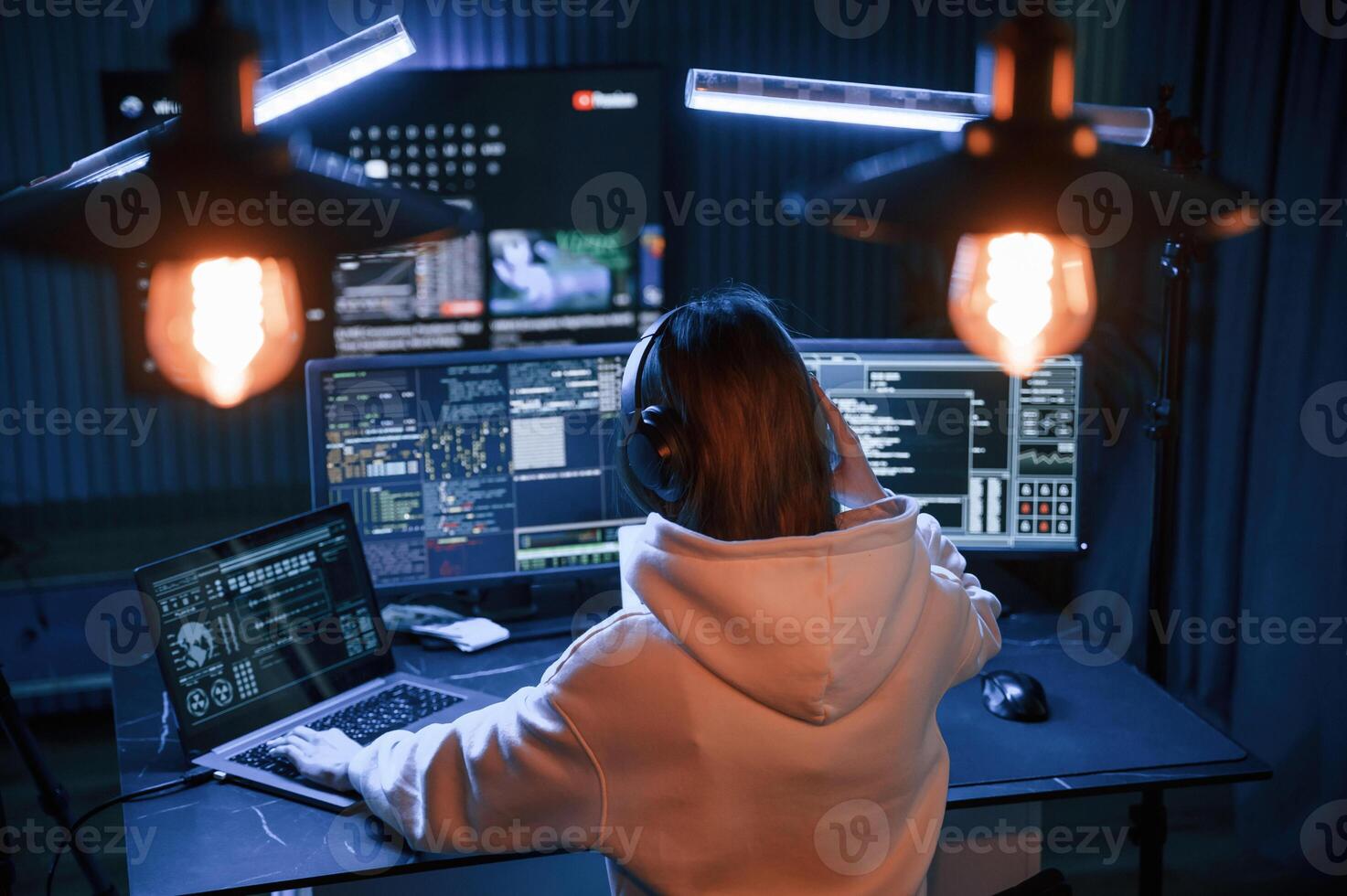 Looking ,at ,screens. Young professional female hacker is indoors by computer with lot of information on displays photo