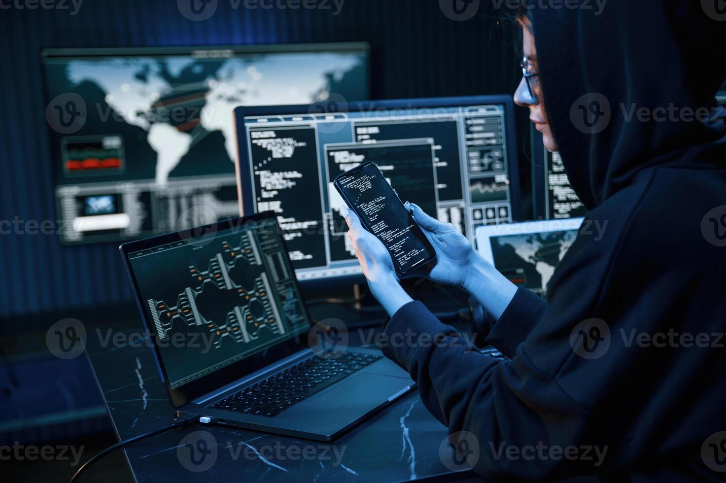 Black colored hoodie. Young professional ,female hacker is indoors by computer with lot of information on displays photo