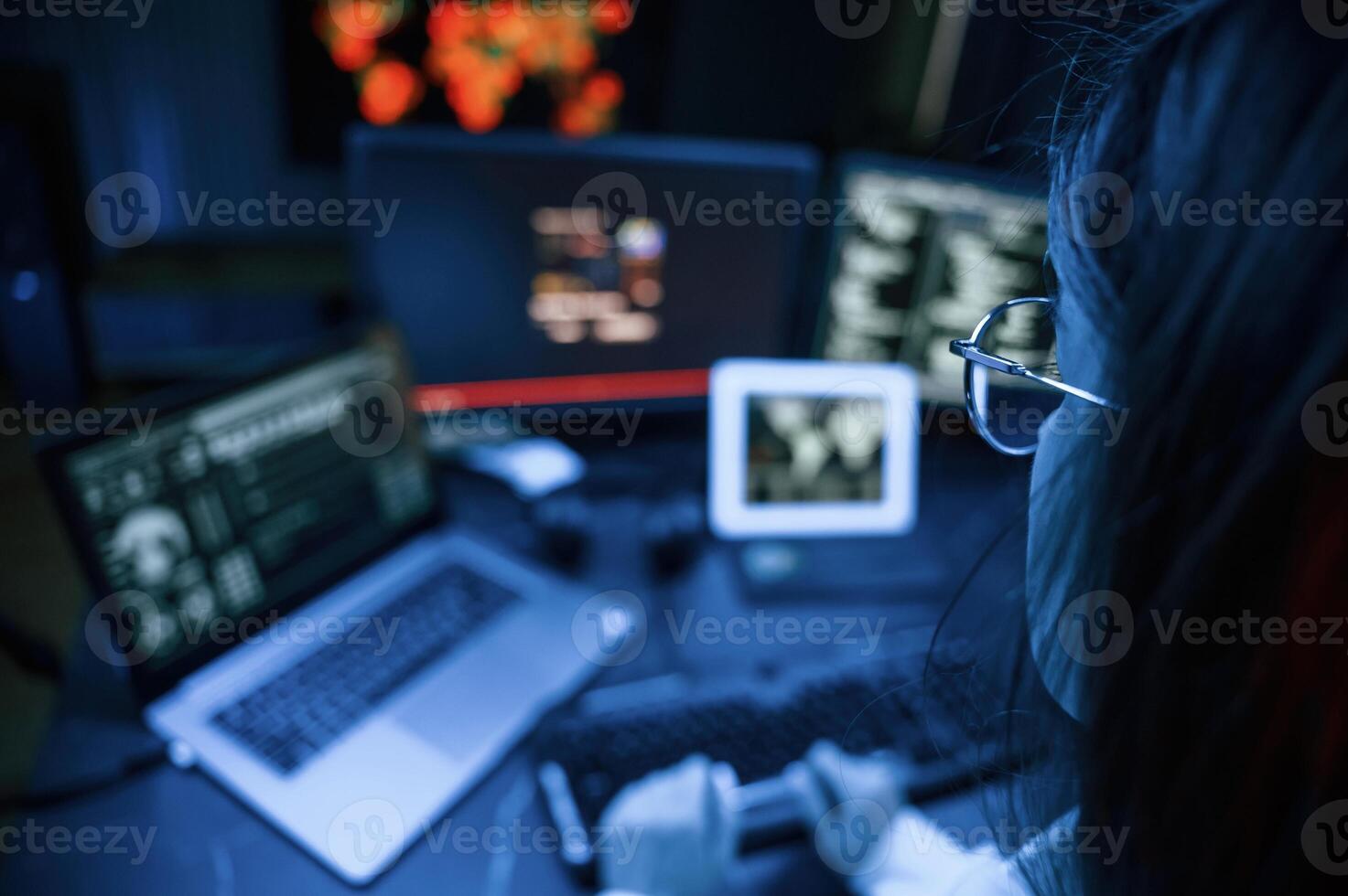Young professional female hacker is indoors by computer with lot of information on displays photo