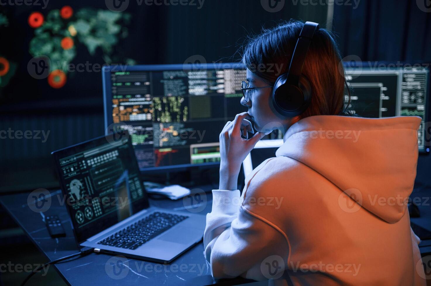 A lot of information on displays. Young, professional, female hacker is indoors by computer photo