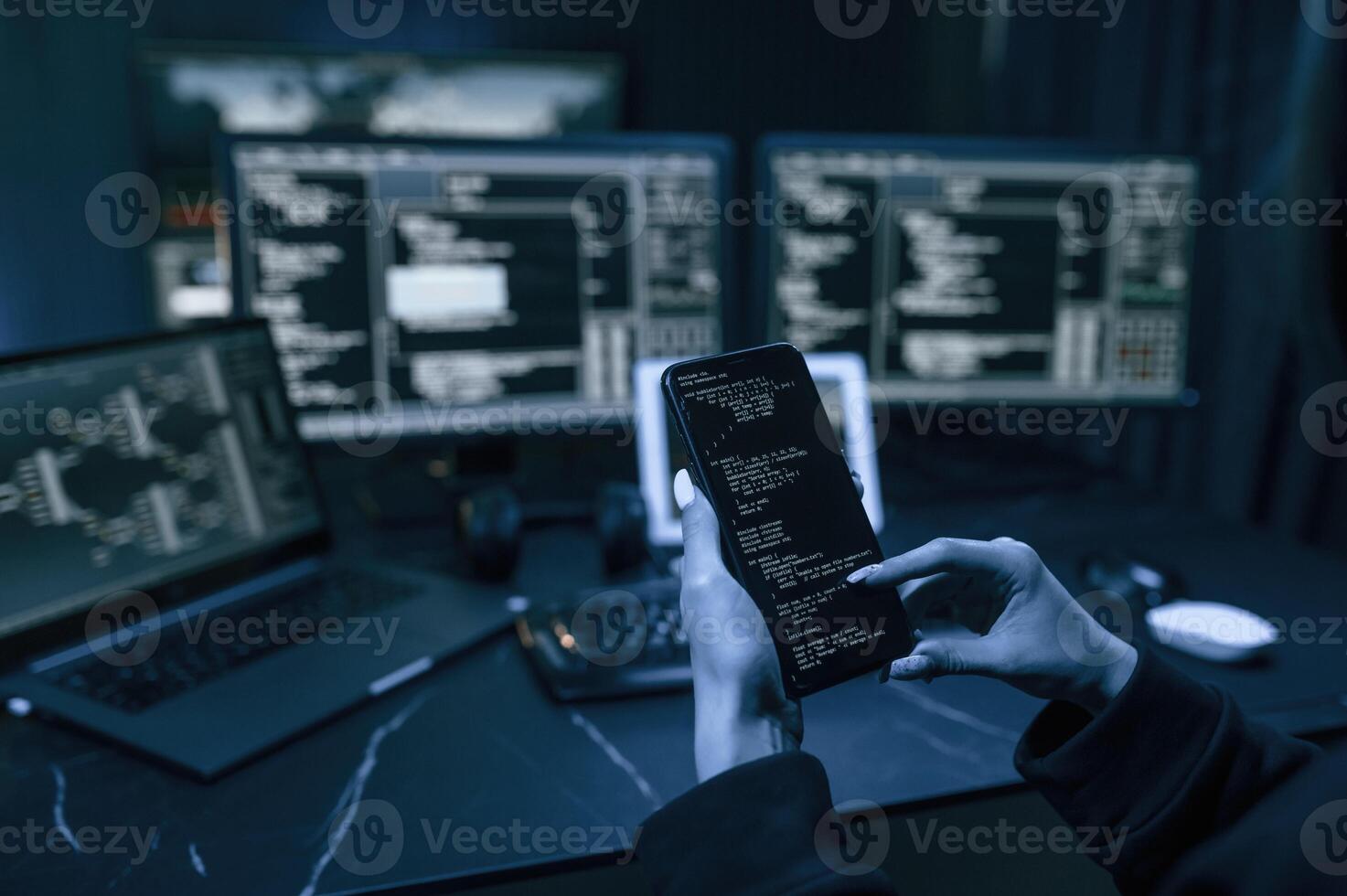 Holding smartphone with code. Young ,professional ,female hacker is indoors by computer with lot of information on displays photo