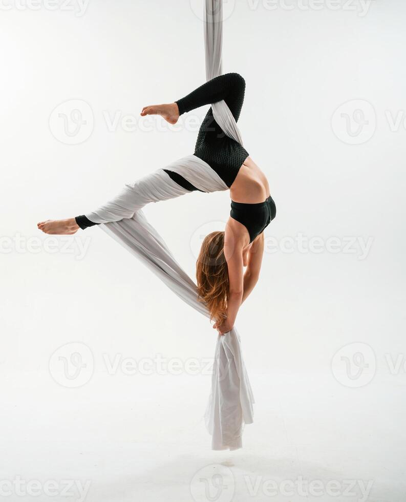 Hanging upside down., Young beautiful woman doing fly yoga against white background photo