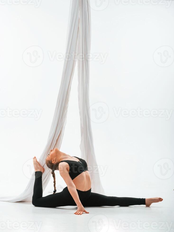 Sitting on the, floor. Young beautiful woman doing fly yoga against white background photo
