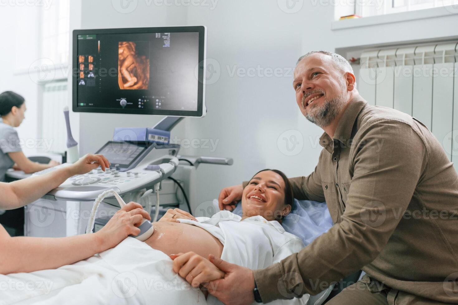 Husband is supporting his wife. ,Pregnant ,woman ,is lying down in the hospital, doctor does ultrasound photo