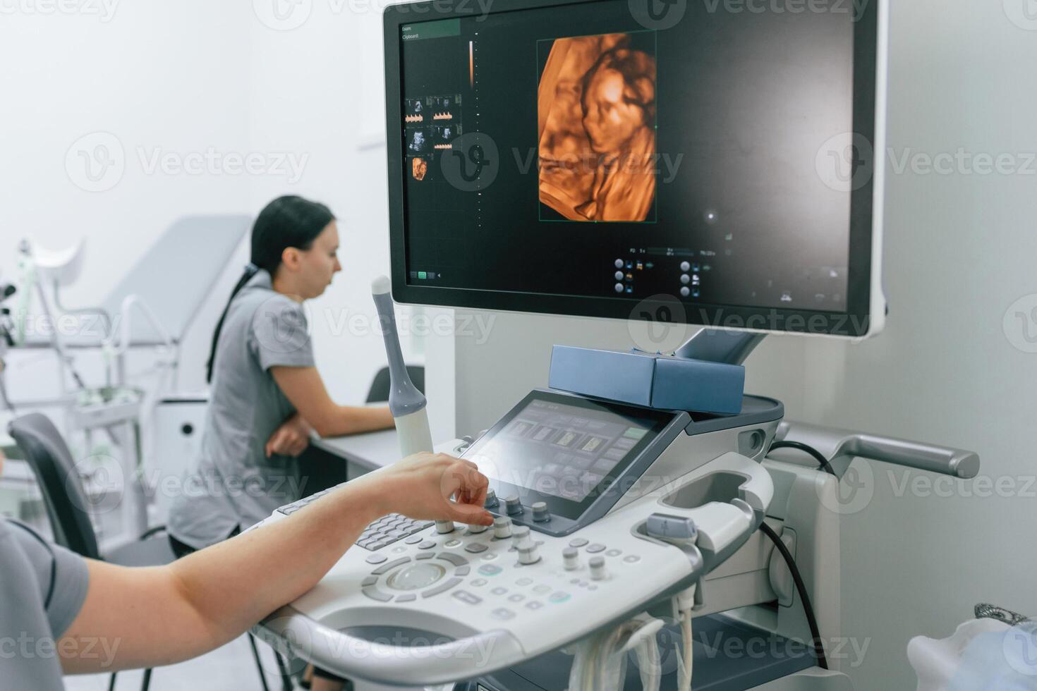 Nurse is working in the clinic, doing an ultrasound scan of the belly of a pregnant woman. Display with little baby photo
