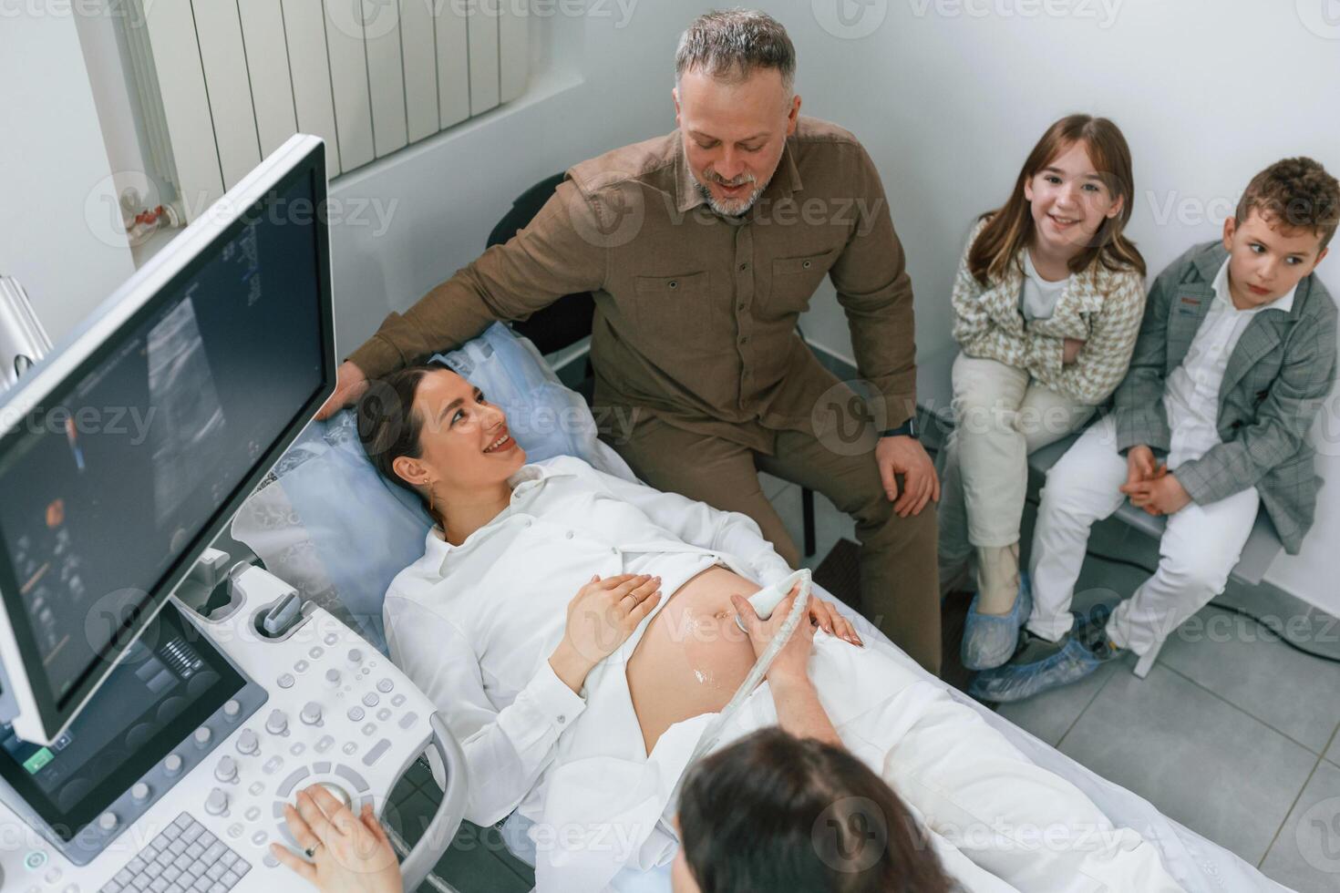 Top view.. Kids ,and ,husband supporting. Pregnant woman is lying down in the hospital, doctor does ultrasound photo