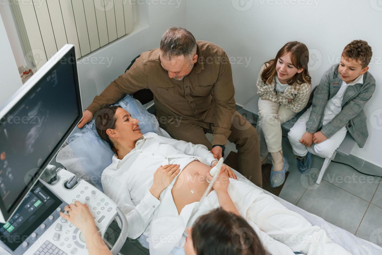 Top view. Kids ,and husband supporting. Pregnant woman is lying down in the hospital, doctor does ultrasound photo