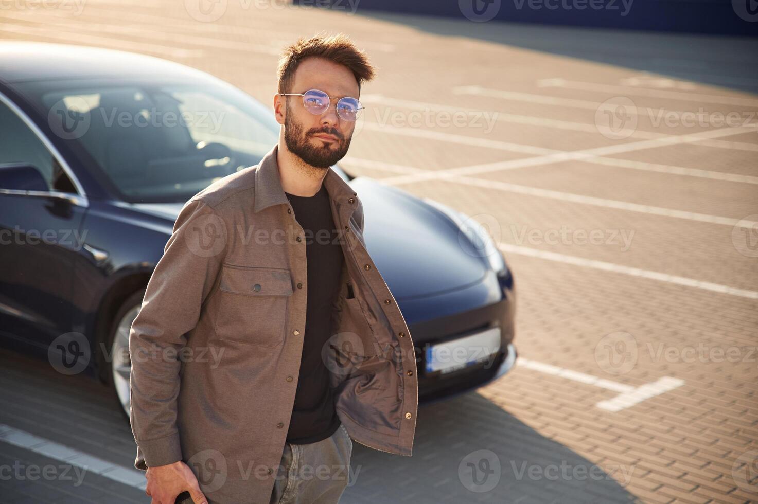 In, glasses.. Man is standing near his electric car outdoors photo