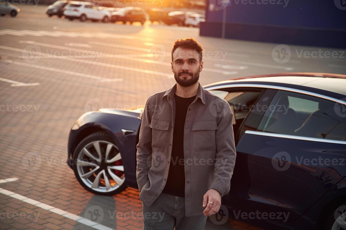 Sunny background. Man is standing, near ,his electric car outdoors photo