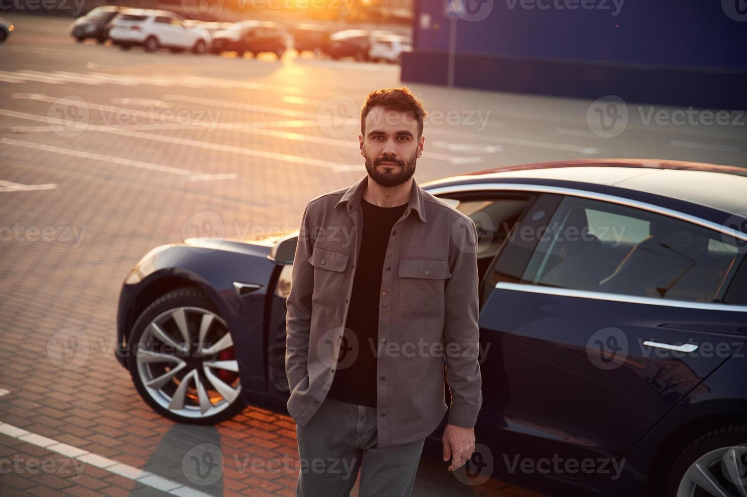Sunny, background. Man is standing near, his electric car outdoors photo