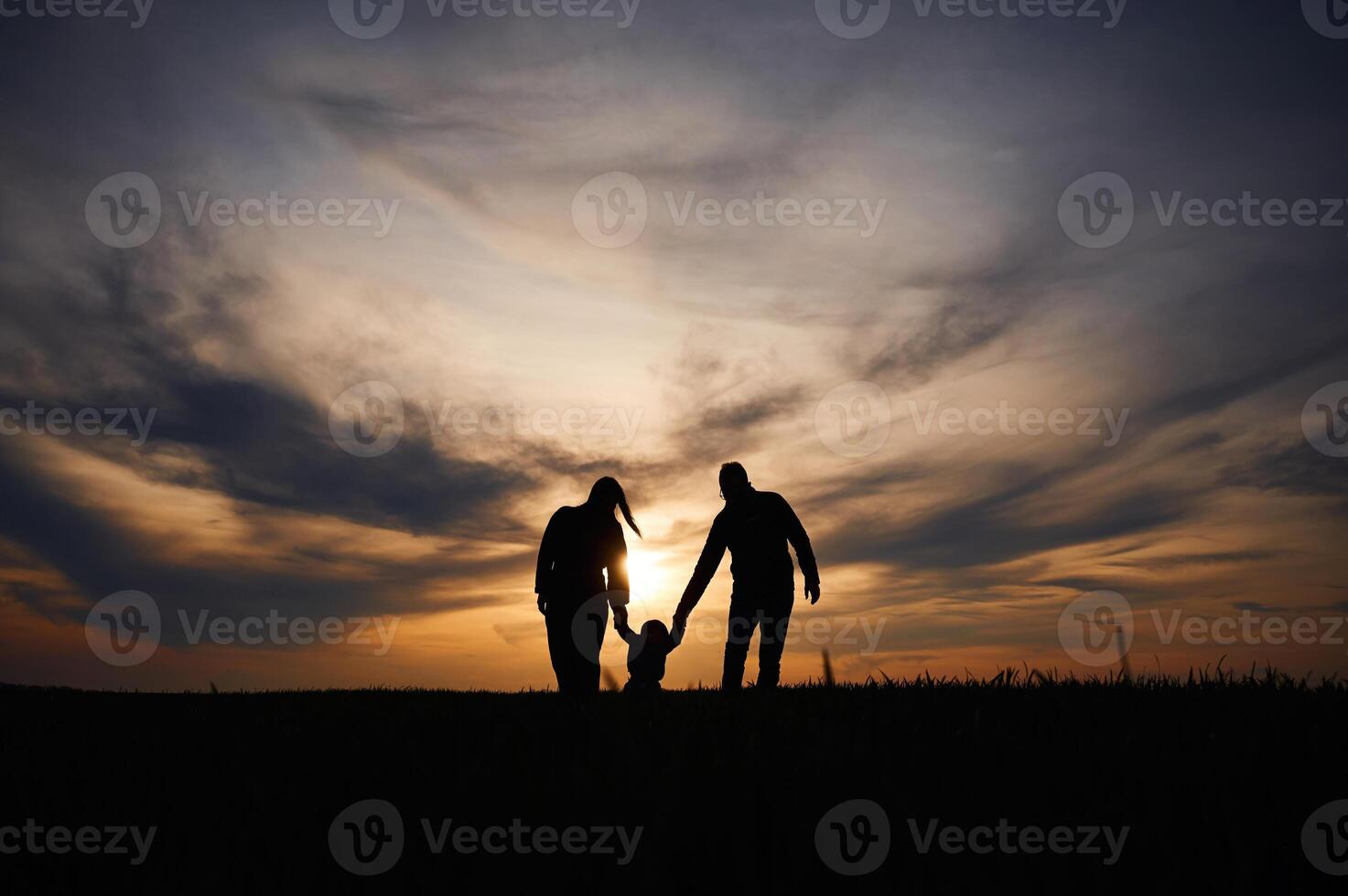 Silhouettes, of father, mother and little baby son is outdoors against sunset dramatic sky in the field photo