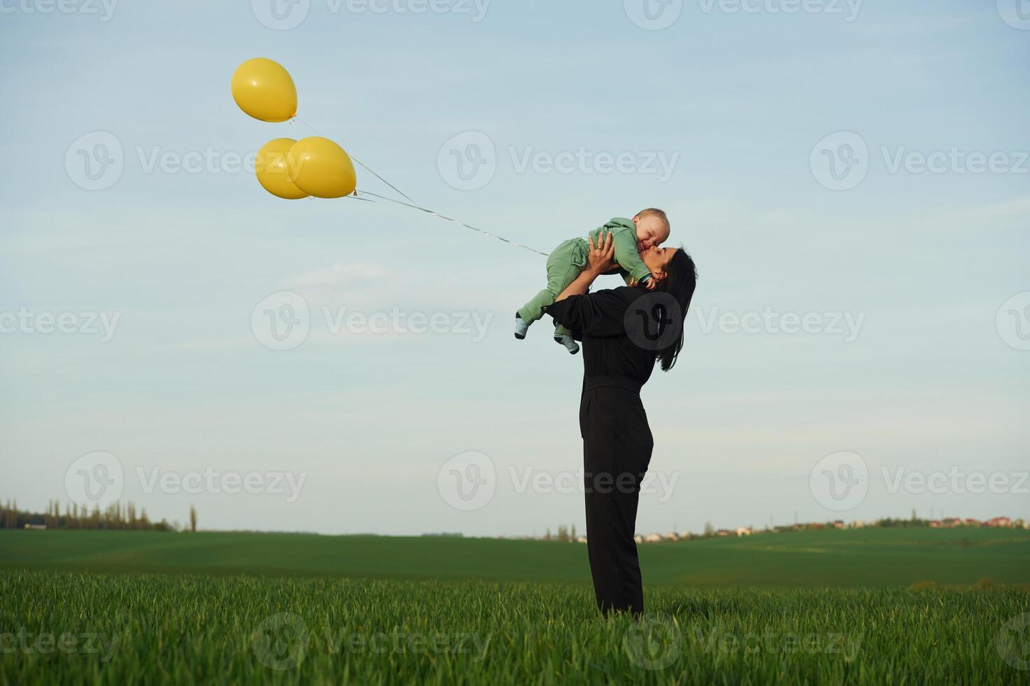 With ,yellow, colored balloons. Mother with her little baby son is outdoors on the agricultural field photo