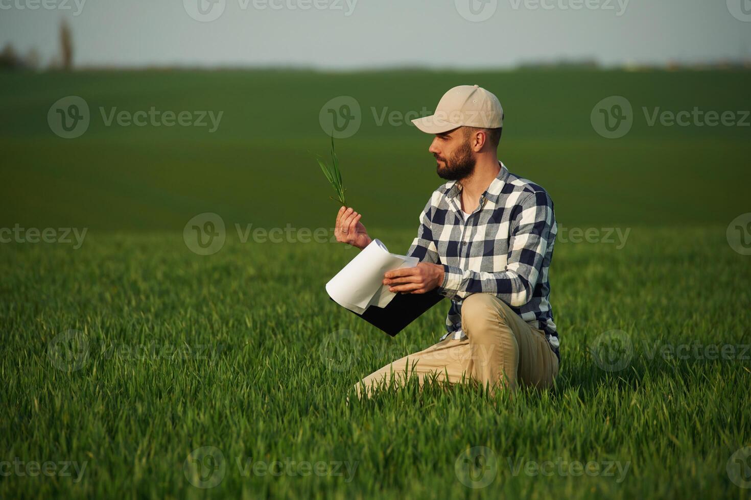 In checkered, shirt ,and with notepad. Handsome young man is on agricultural field photo