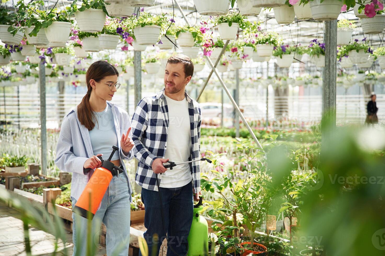 Walking, looking, at, each other, holding watering device. Florist man and woman are together in greenhouse photo