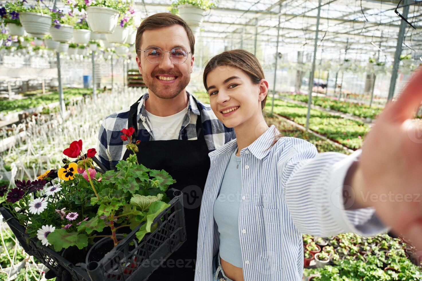 Making selfie, smiling. Florist ,man and woman are working together in bright greenhouse photo