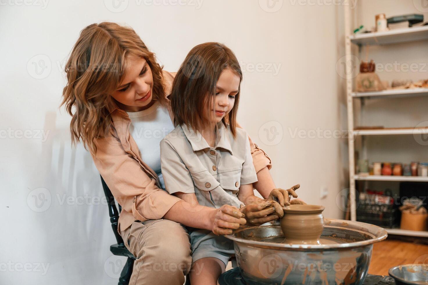 Using c,lay to, create,the pot. Mother with little girl learning pottery in the workshop photo