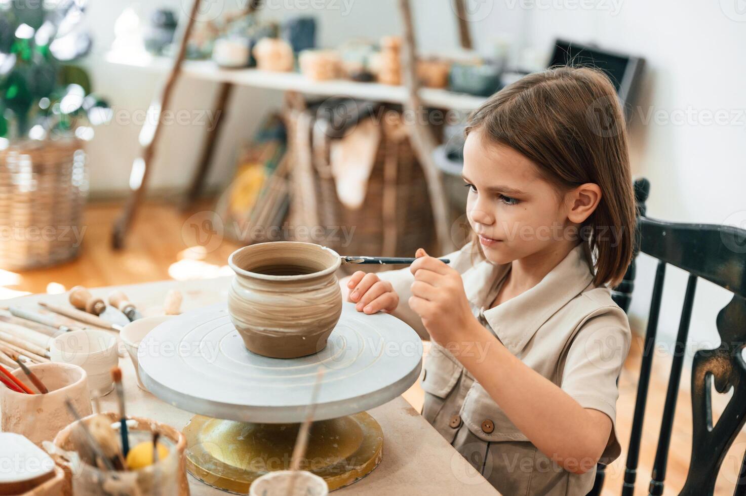 Painting ,the pot by, brush. Little girl is learning how to do pottery in the workshop photo