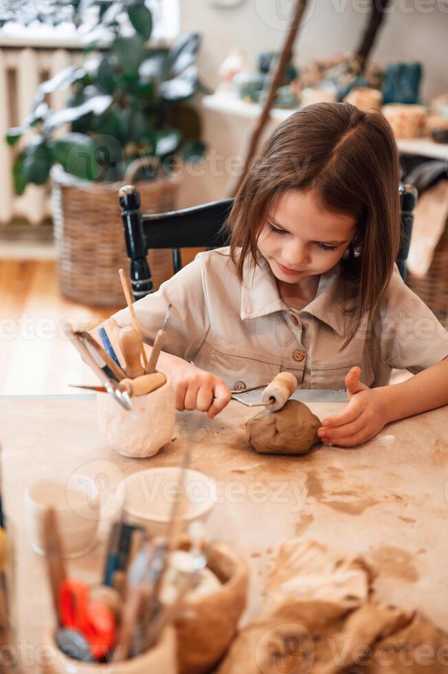 Working with clay. Little,, girl is learning how to do pottery in the workshop photo