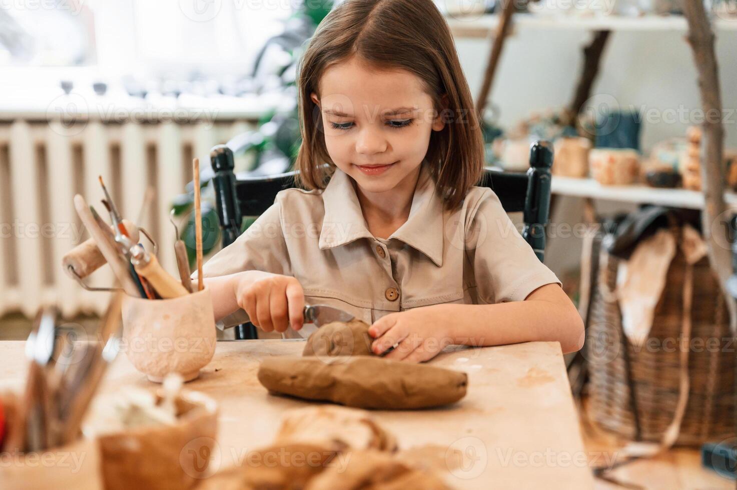 Working, with clay, Little girl is learning how to do pottery in the workshop photo