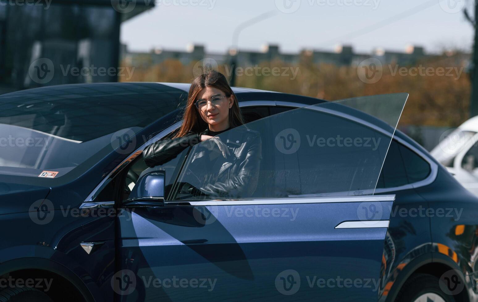 Young woman is near ,her, electric car outdoors photo