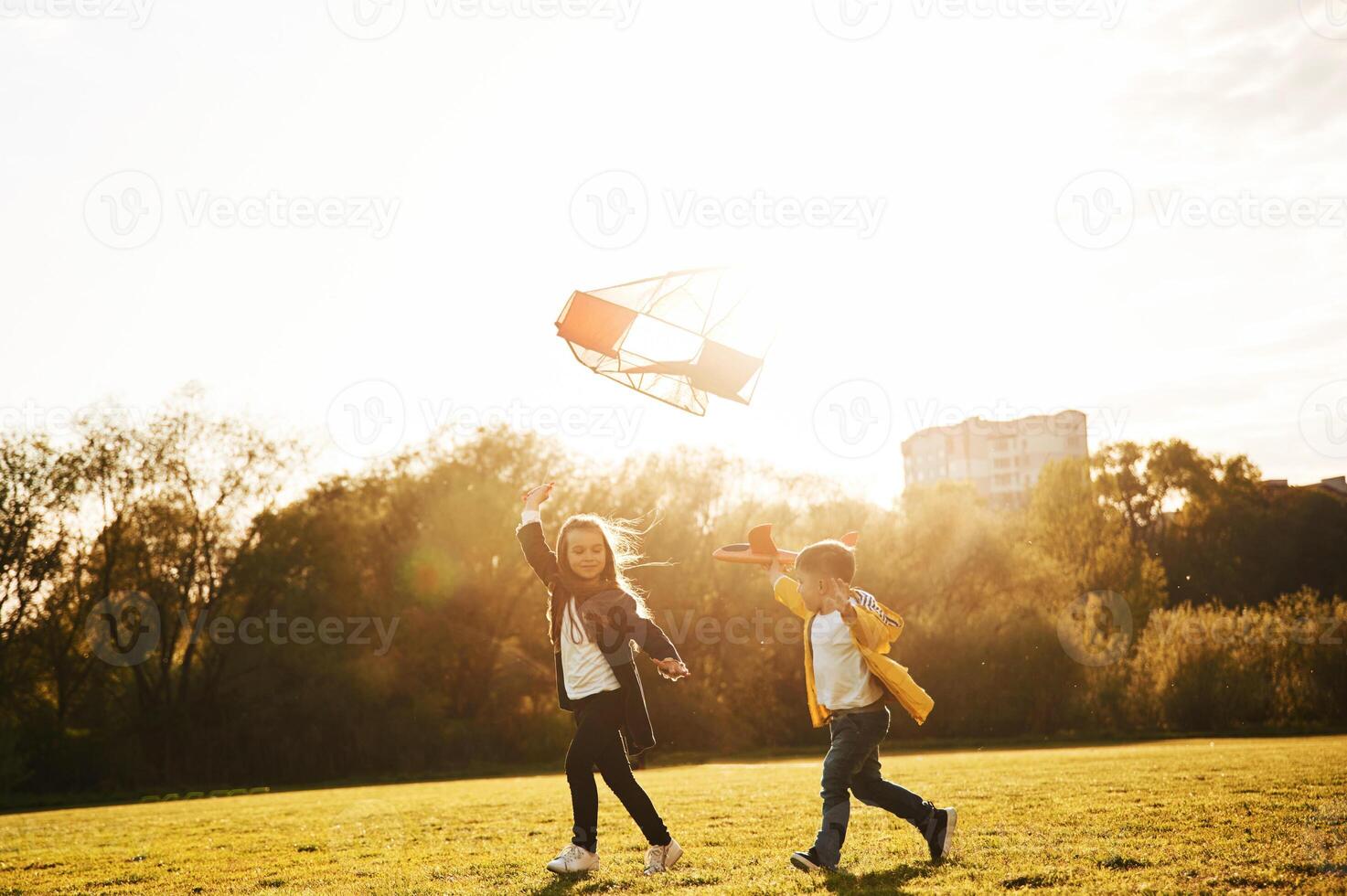 Running together. ..Two kids are playing with kite on the summer field photo
