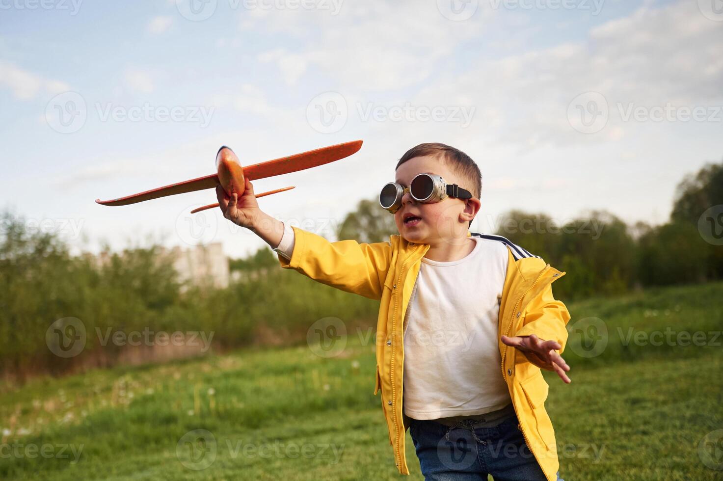 Aviator glasses are ,worn. Little boy is playing with toy plane on the summer field photo