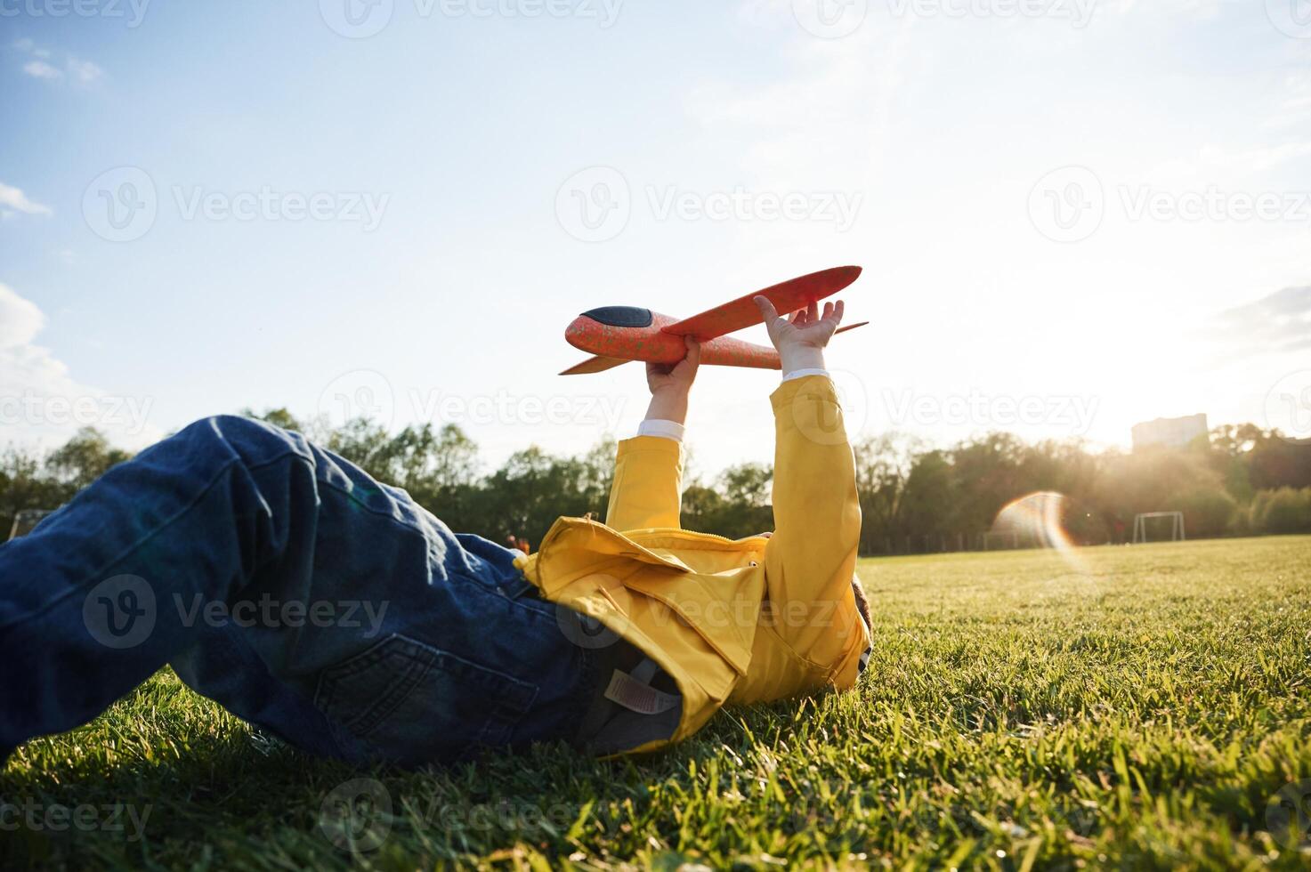 Lying down on ground.. Little boy is playing with toy plane on the summer field photo