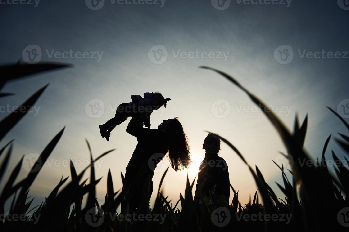 Silhouette of, woman that holding her daughter in hands. Another girl is standing and watching photo