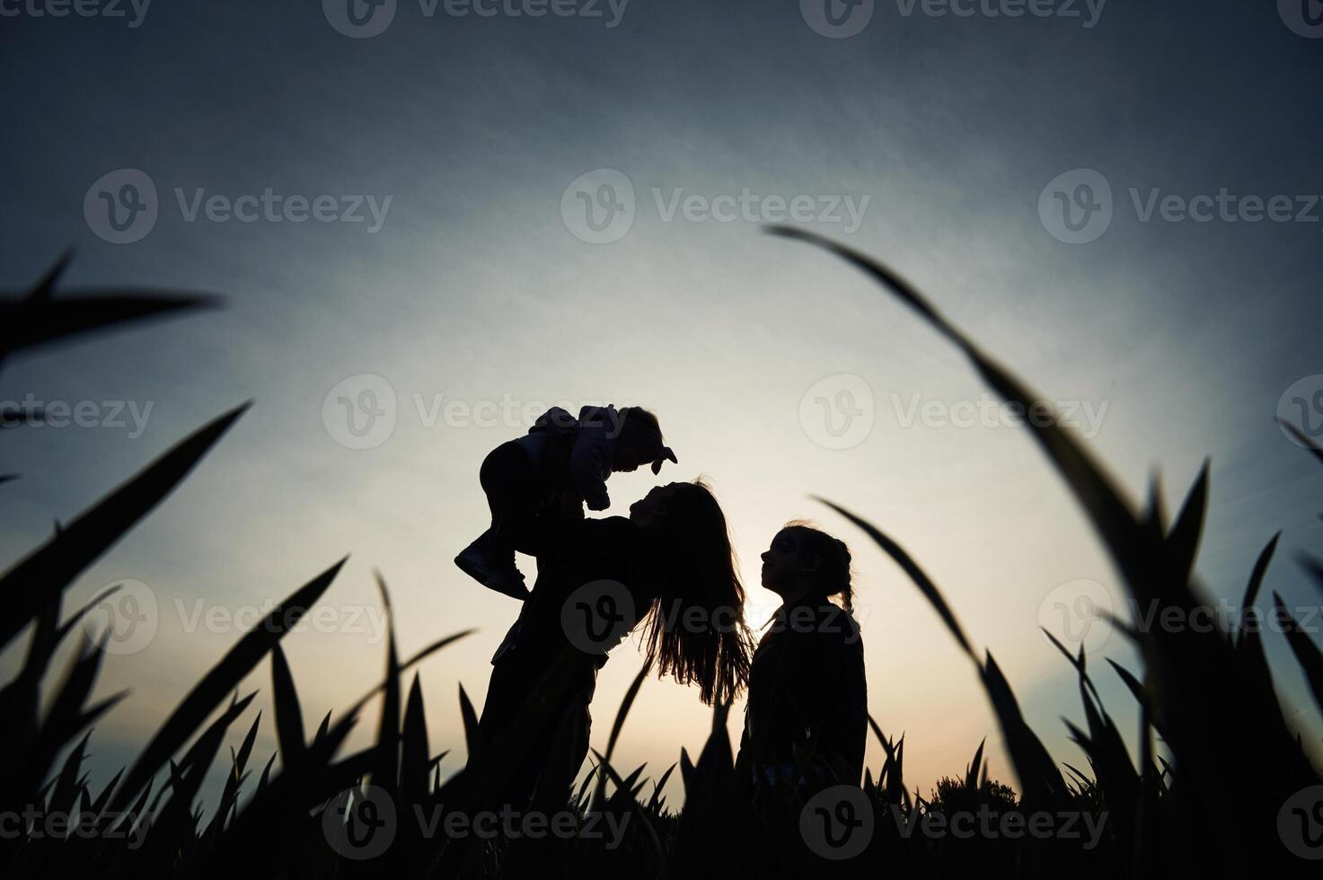 Silhouette of woman that holding her daughter in hands. Another girl is standing and watching photo