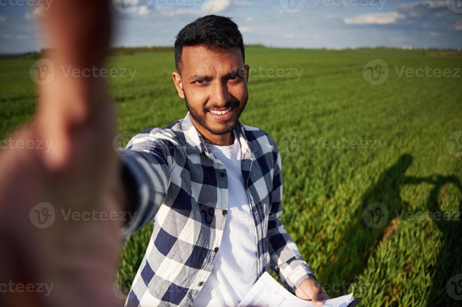 Making selfie, holding notepad. Handsome Indian man is on the agricultural field photo