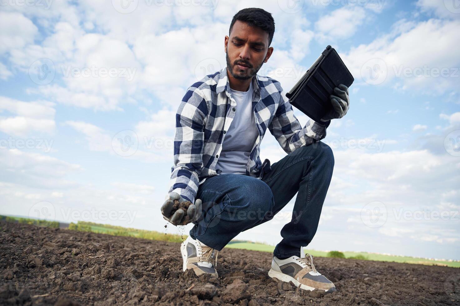 Conception of quality control, with digital tablet. Handsome Indian man is on the agricultural field photo