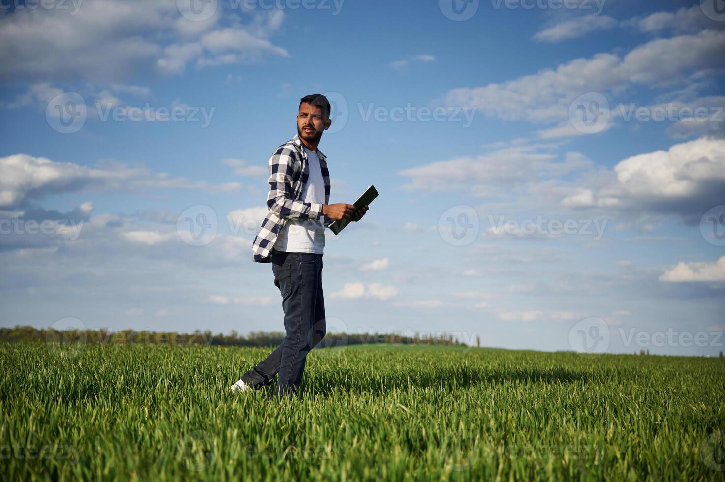 Standing,, and holding notepad. Handsome Indian man is on the agricultural field photo