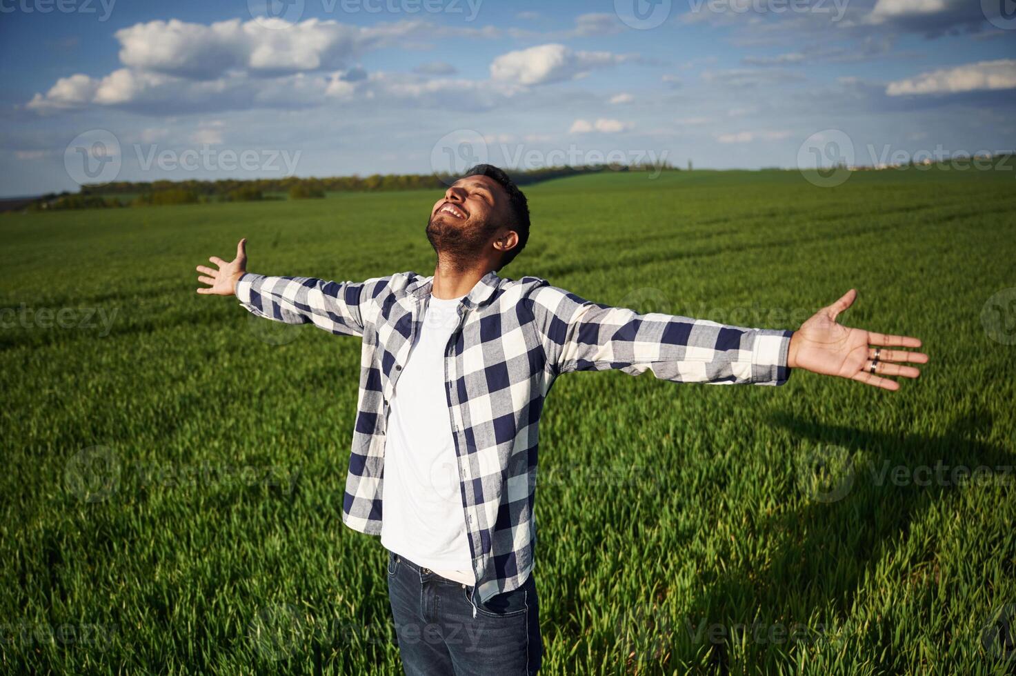 Enjoying ,,freedom, smiling, hands on the sides. Handsome Indian man is on the agricultural field photo