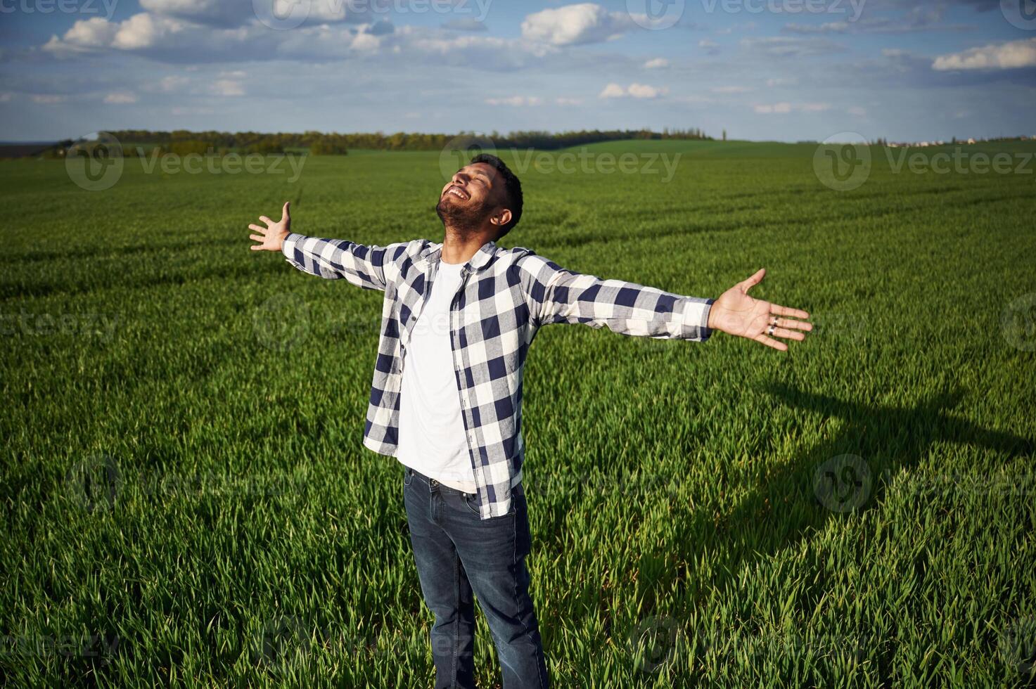 Enjoying, freedom, smiling, hands on the sides. Handsome Indian man is on the agricultural field photo