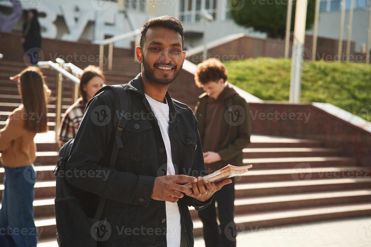 Indian man is standing in front of his friends. Four young students in casual clothes are together outdoors photo