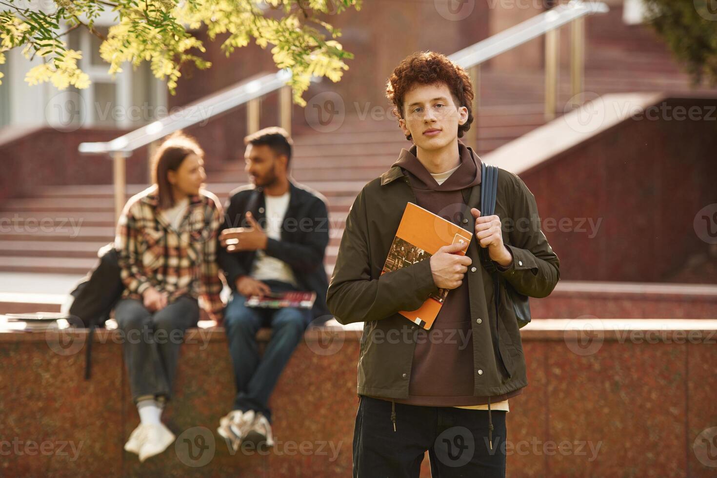 With, yellow ,colored notepad. Young students in casual clothes are together outdoors photo