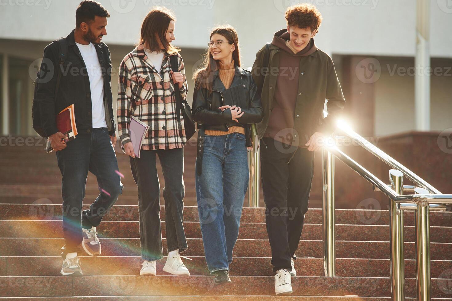 Walking,,, holding notepads.. Four young students in casual clothes are together outdoors photo