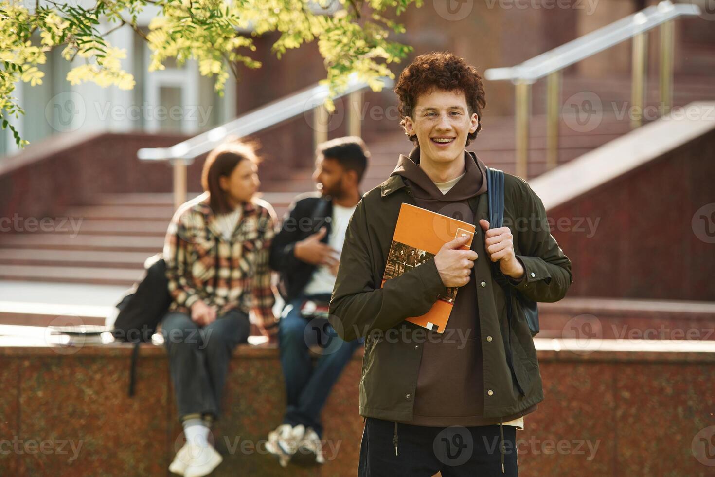 With yellow colored notepad.,. Young students in casual clothes are together outdoors photo